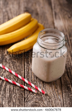 Delicious banana smoothie in glass jar with drinking straw and bananas on table.
