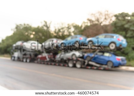 Blurred image big car carrier truck of new cars for batch delivery to dealership. Full load transport truck of new vehicles on country road in San Antonio, TX. Automotive industry abstract background.
