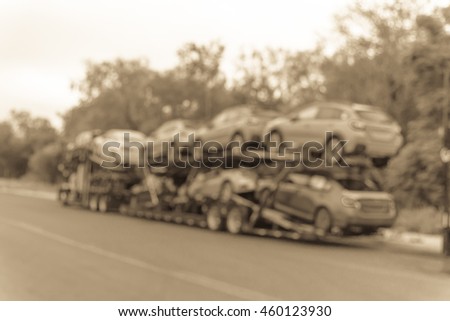 Blurred image big car carrier truck of new cars for batch delivery to dealership. Full load transport truck of new vehicles on country road. Automotive industry abstract background.Vintage filter look