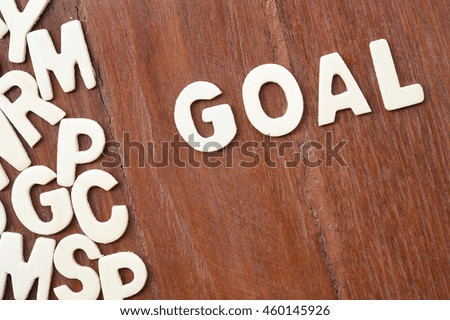 Word goal made with block wooden letters next to a pile of other letters over the wooden board surface composition
