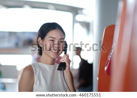 soft focus on a beautiful woman feel happy while using public telephone for talking with her friend and blurry background of people 