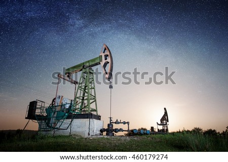 Oil pumps are working on the oil field in the evening under night sky with stars. Milky way. Oil industry equipment
