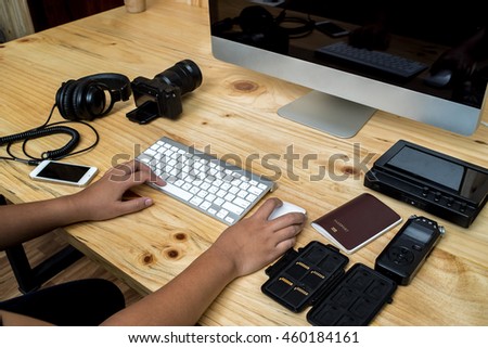 Office computer PC camera, mobile phone, headphone,sound recorder,passport,memory card,keyboard and mouse on wooden desk, Asian women hands photo editor working on computer 
