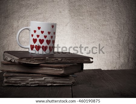 Old books and mug with many pictured hearts on the old wooden table. Toned.