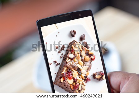 Closeup of hands making photo of sweet dessert on mobile phone while sitting in restaurant, and focus at a sliced brownie cake on the white plate