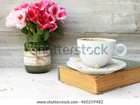 Full light composition with cup of fresh tasty coffee, vintage book with yellow shabby cover and paper and bunch of pink flowers. Concept for beautiful romantic morning theme with retro decor elements