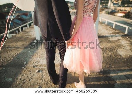 Pretty sunny outdoor portrait of young stylish couple while kissing on the roof with city view