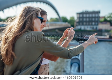 Two girls taking picture of the cityscape. River in the background