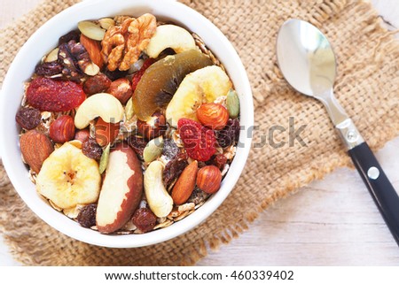 Top view of a healthy bowl of muesli mixed with dried fruit and nuts on a wooden background.