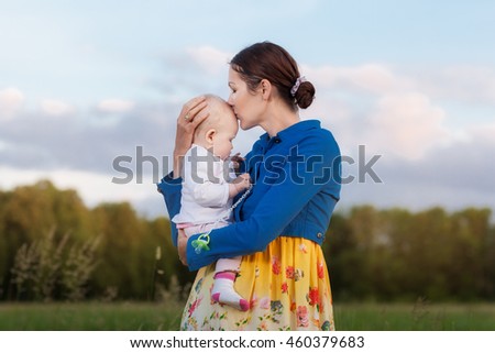 Mom holds daughter on hands. They stand in a meadow. Mother kissing daughter