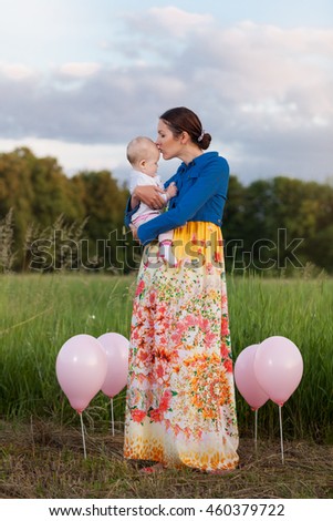 Mom and daughter on the field among the balloons. Mother kissing daughter