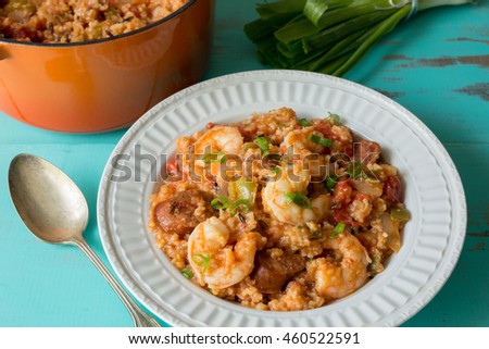 White textured bowl filled with shrimp and sausage Jambalaya. Shown on turquoise table with vintage silver spoon and orange cast iron stock pot. 