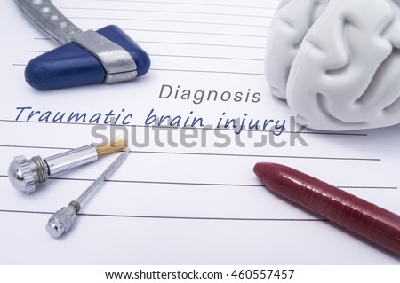 Figure of human brain, blue neurological reflex hammer, neurological needle and brush for test sensitivity and ballpoint pen lie on a paper form with a medical diagnosis of Traumatic brain injury