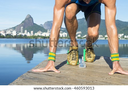 Track athlete with gold shoes crouching in starting blocks in front of the Rio de Janeiro skyline at Lagoa Rodrigo de Freitas lagoon