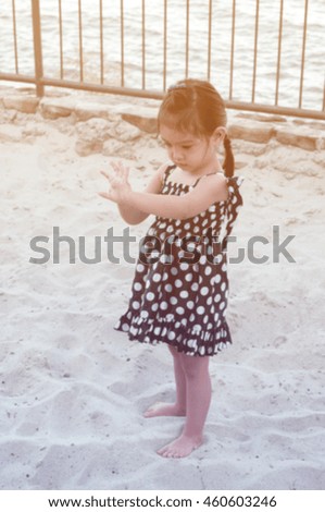 blurred pictured of long hair toddler girl wearing little black dress playing sand by lake, vintage filtered color tone