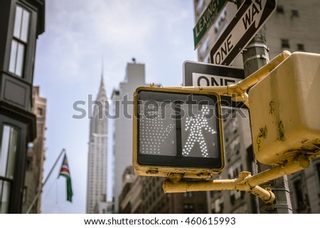 Yellow NYC crosswalk sign on busy one way street with skyline in the background.