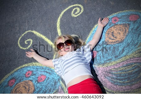 Funny little girl lying on asphalt with painted butterfly wings. Concept of a imagination 