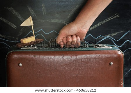 hand takes the handle of a suitcase with a retro ship in the background painted with chalk sun / time to to travel and cruises