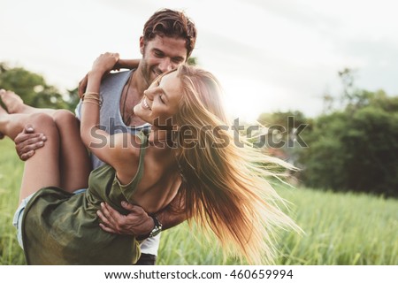 Shot of young woman being carried by her boyfriend in grass field. Couple having fun on their summer holiday. Royalty-Free Stock Photo #460659994