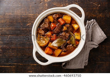Beef meat stewed with potatoes, carrots and spices in ceramic pot on wooden background Royalty-Free Stock Photo #460693750