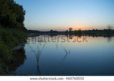 Summer evening at the river. Quiet and calm evening. The sun slowly sinks below the horizon. Around serenity. It is a natural landscape. Sunset and twilight.