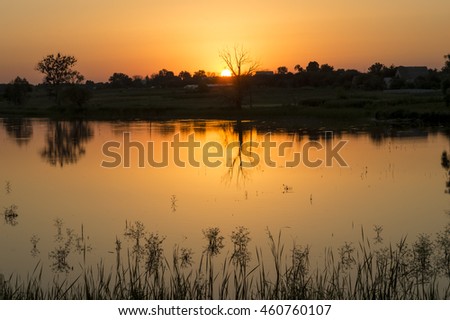 Summer evening at the river. Quiet and calm evening. The sun slowly sinks below the horizon. Around serenity. It is a natural landscape. Sunset and twilight.