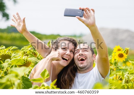 young happy couple man and woman are in a field of sunflowers, make selfie pics, grimace and fun