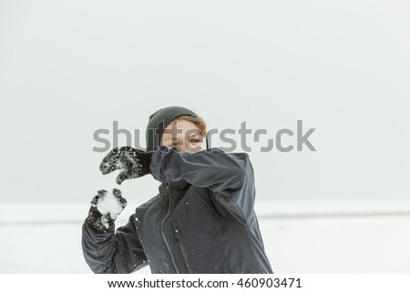 Waist Up of Young Teenage Boy Wearing Jacket and Knitted Hat Throwing Snowball and Choosing Target Outdoors on Overcast Winter Day