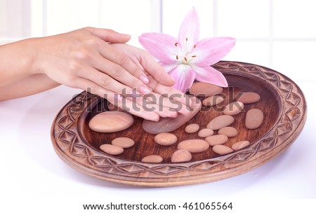 Closeup photo of a woman's hands in the bowl with water and spa stones and pink lily flower, body part, beauty treatment in a spa salon