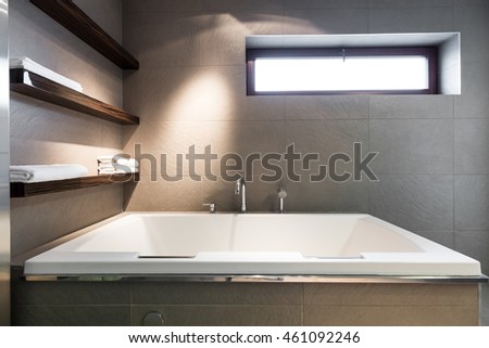 Modern, minimalist bathroom with a large, square bath, towel shelves and a rectangular window