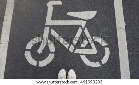 The bicycle sign on the grey road with white shoes standing in the public park for biking