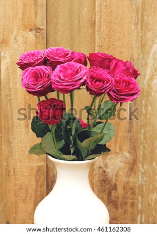 Bunch of beautiful pink roses in vase against a wooden background