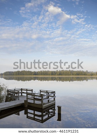 Silent morning by the lake. An image of an empty pier during sunrise from the back. The sun is coloring up the sky and the forest across the lake.