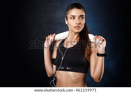Young beautiful sportive girl listening music over dark background.
