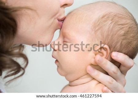 Funny newborn babe napping in mom arms. Young mother kissing sleeping adorable new born child on the forehead. Healthy little kid in parent arms. Love, bonding, happy family concept. Indoor. Close-up