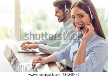 Side view of beautiful young business woman and handsome businessman in headsets using laptops while working in office. Girl is looking at camera Royalty-Free Stock Photo #461245441