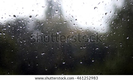 Close-up of water droplets on glass. Rain drops on window glass with blur background. Blurred tree and sky. Rainy days, rain running down window, bokeh