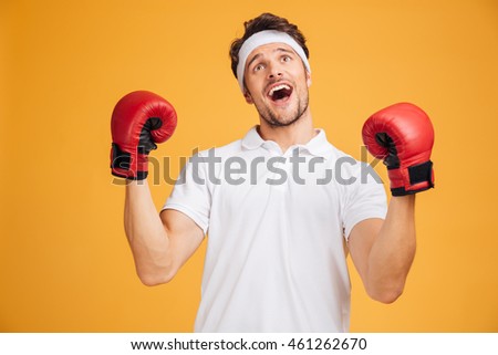 Cheerful excited young man boxer in red gloves shouting and celebrating success over yellow background