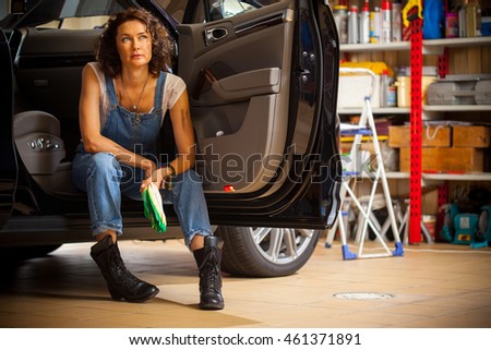 Portrait of a handsome mechanic in blue overalls with a gloves in his hand on the threshold of the car with an open cabin door in repair car workshop