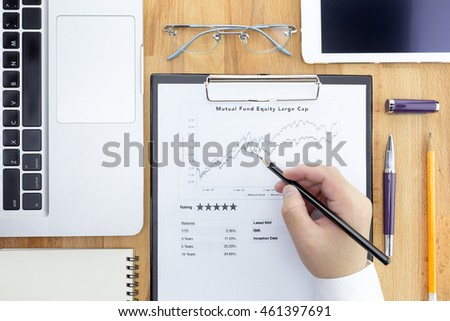 Businessman or Fund manager review Mutual Fund information with performance line graph and benchmark. Fund performance with glasses, digital tablet, pen, pencil, computer laptop. Flat lay.