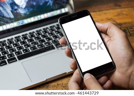 Close up hand holding smart phone with laptop on wood desk.  Smartphone with blank screen and can be add your texts or others