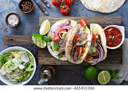 Steak tacos with sliced meet, salad and tomato salsa on a cutting board