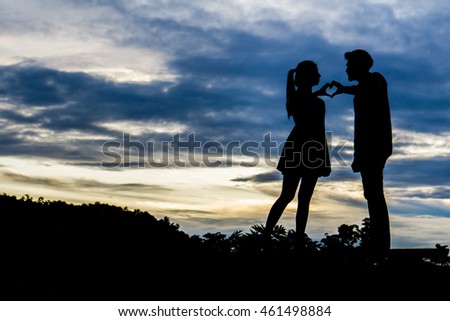 Sunset silhouette of young couple in love , Heart-shape conceptual symbol for love .