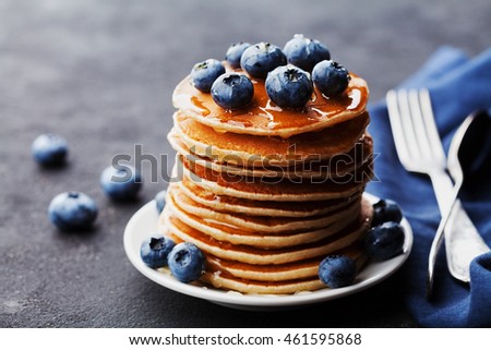Stack of baked american pancakes or fritters with blueberries and honey syrup on rustic black table. Delicious dessert for breakfast. Royalty-Free Stock Photo #461595868
