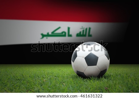 vintage black and white football ball on green grass has the national flag of iraq background
