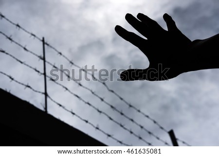 Silhouette hand extending to the sky with defocus barbwire, on gloomy overcast sky