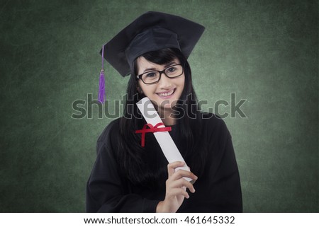 Photo of happy female bachelor smiling in the class while wearing graduation cap and holding certificate