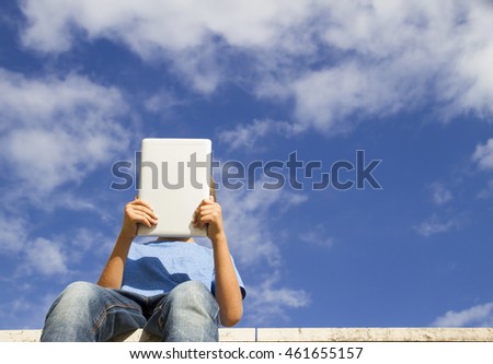 Boy with tablet PC sitting against blue sky. Low angle view. People, technology, education, leisure concept