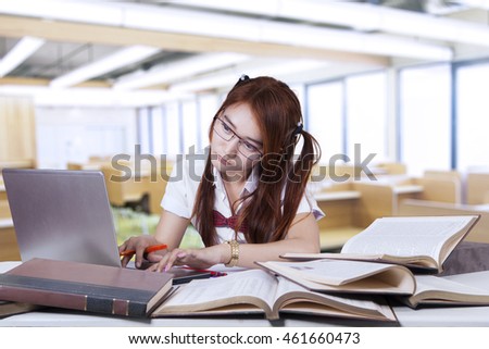 Female college student studying in the class while typing on the laptop computer with books on desk