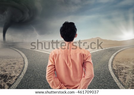 Back view of a young businessman looking at two different road with storm and bright sunlight